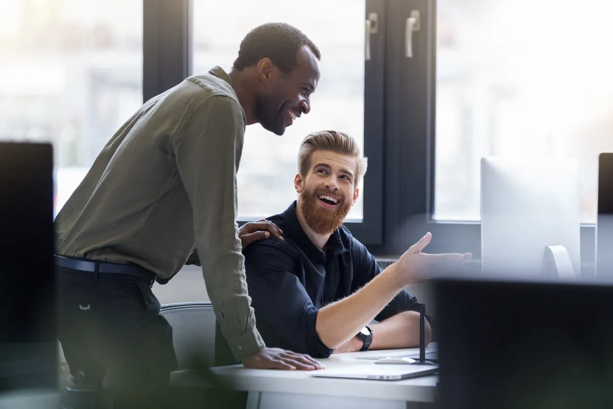 Two professionals collaborating at a desk in a modern office, smiling and engaged — the candid, hands-on coordination that the partner network is built around.